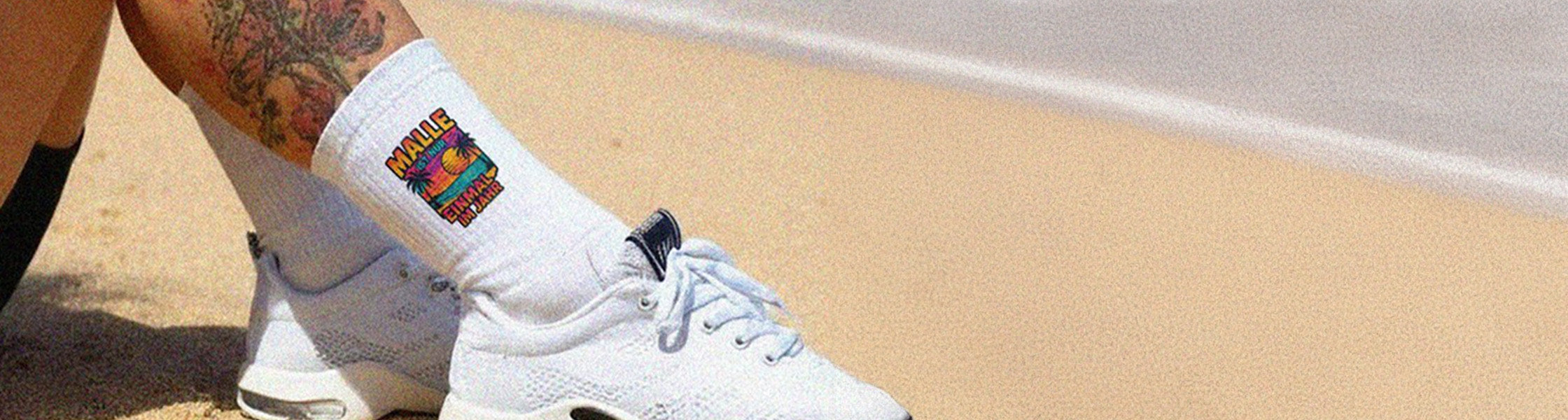 Person trägt bedruckte Socken mit buntem Motiv am Strand – Kontakt und Hilfe bei Sockenprinz.